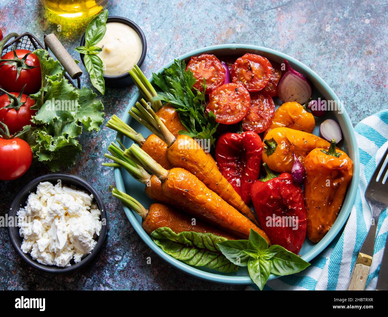 baked grill baby carrots, tomato, bell pepper in a plate, basil and spices vegan dish, close up, white sauce, goat cheese Stock Photo