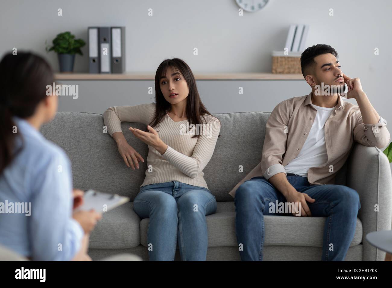 Unhappy arab woman talking about problems and breakup with professional marriage consultant, husband listening Stock Photo