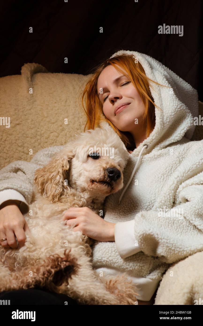 woman lies with a large dog on the couch. The shaggy domestic dog laid its head. The relationship of animals and people at home. Stock Photo