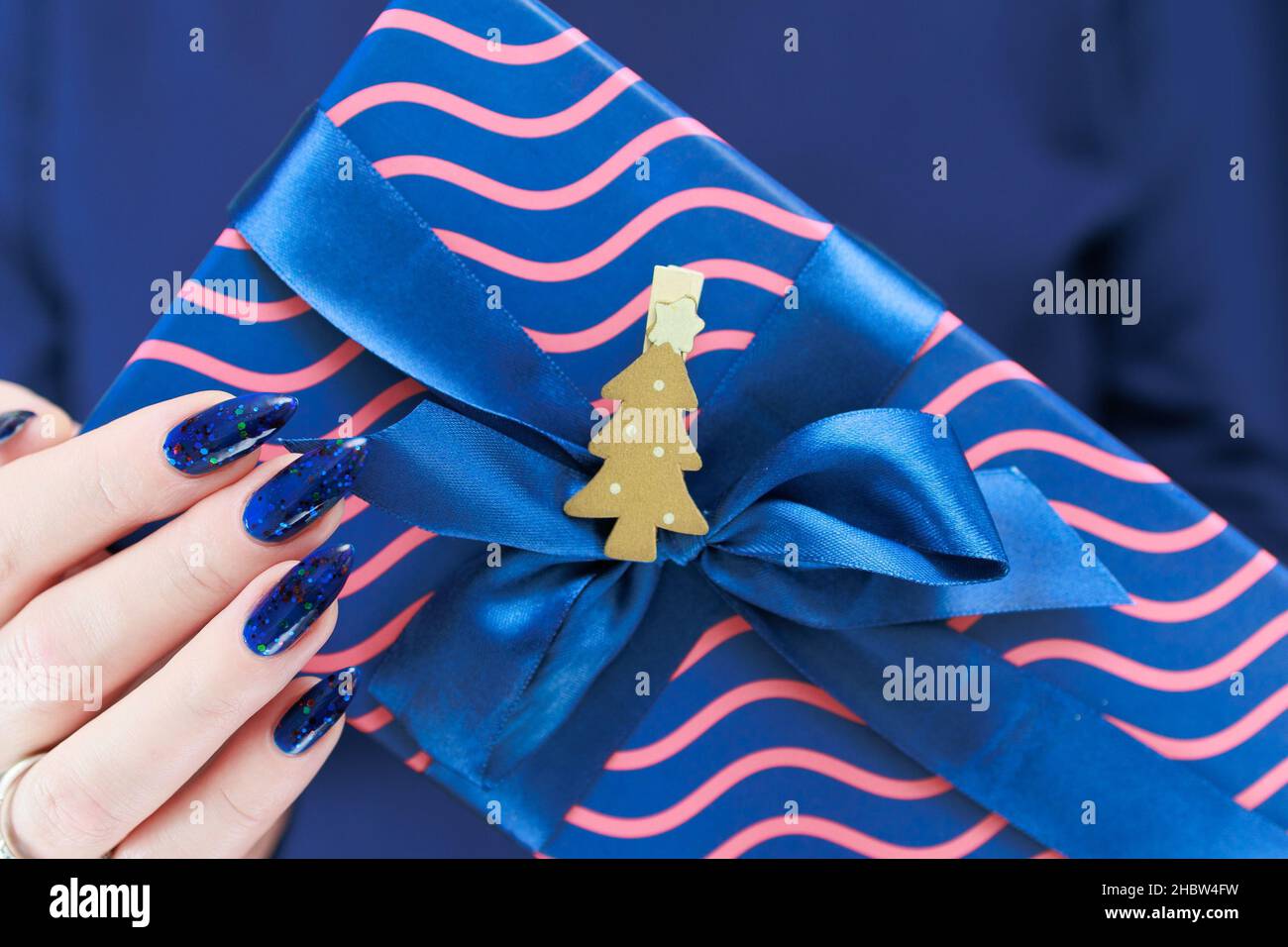 Female hands with blue manicure hold a gift box for New Year and Christmas. Stock Photo