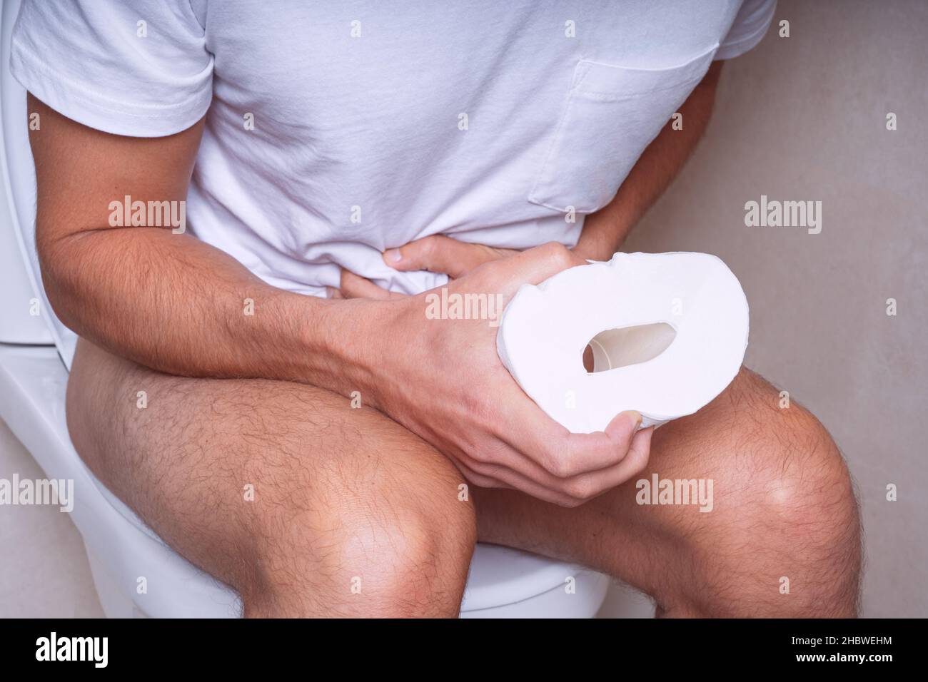 Man sitting on the toilet and suffering from stomach pain, constipation, diarrhoea or stomach cramps Stock Photo