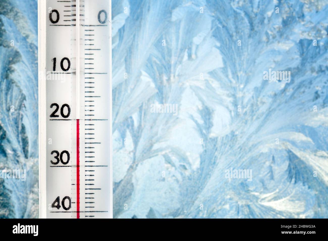 The thermometer shows a low temperature of minus 20 Celsius. Weather forecast. A frosty day and ice patterns on the glass Stock Photo