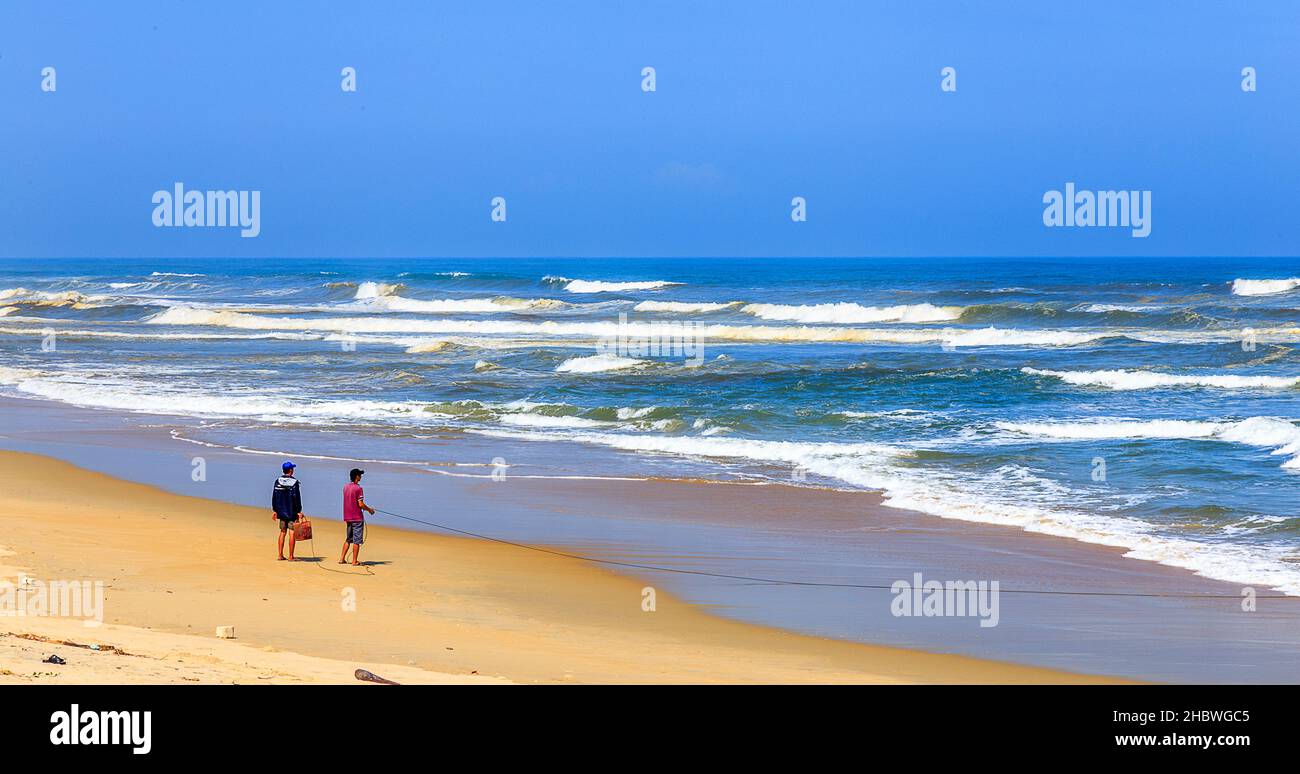 Two people on the beach one with a line going out to the water controlling a net. Stock Photo