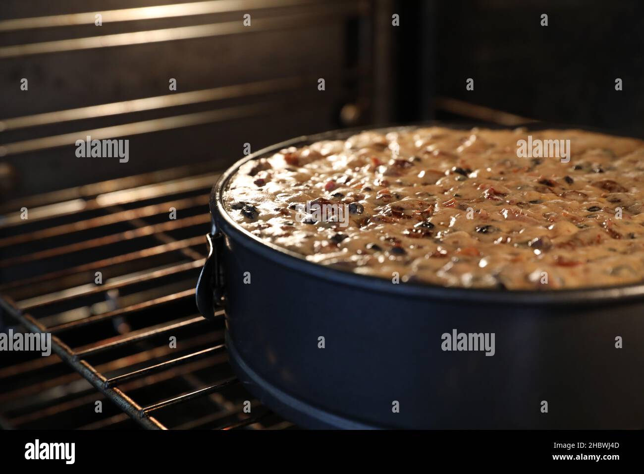 A close up large round traditional Christmas cake in the oven slowly baking or cooking. A variety of fruit visible on the still wet moist surface. Stock Photo
