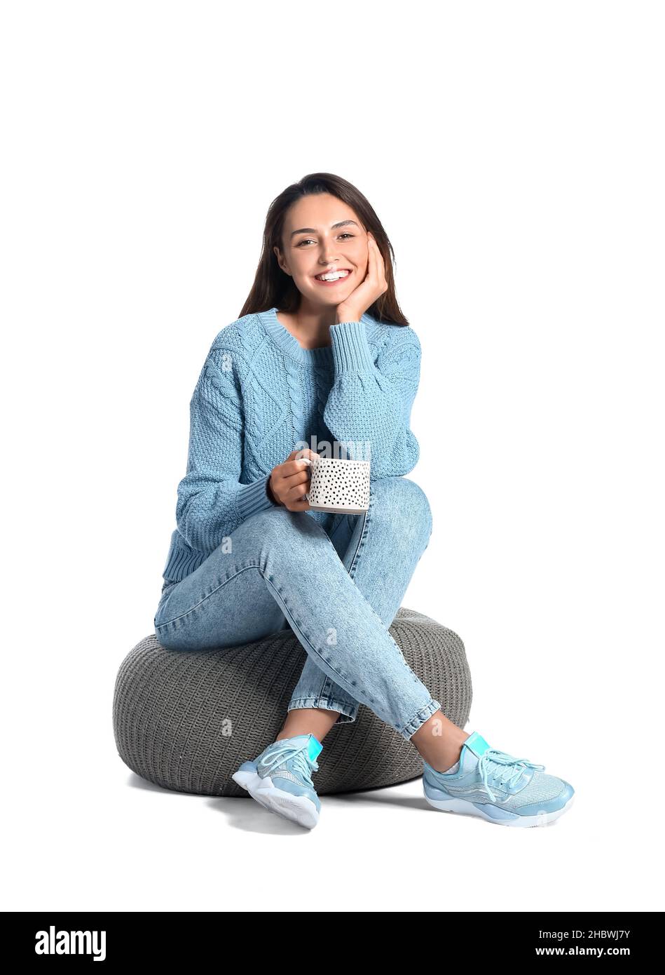 Beautiful woman with cup of coffee sitting on pouf against white ...
