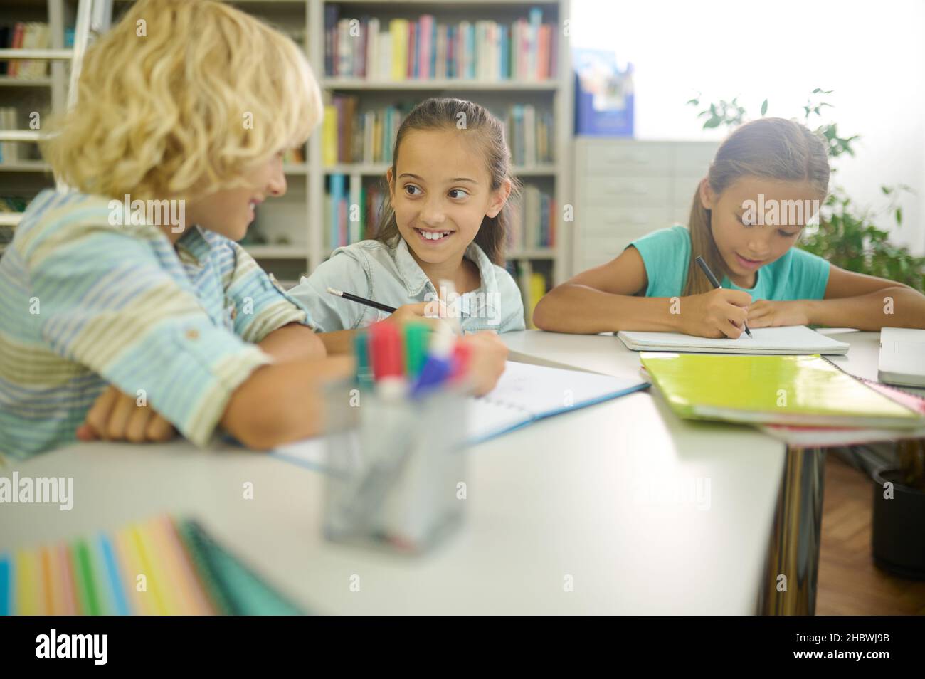 Girl looking at boy writing at table Stock Photo