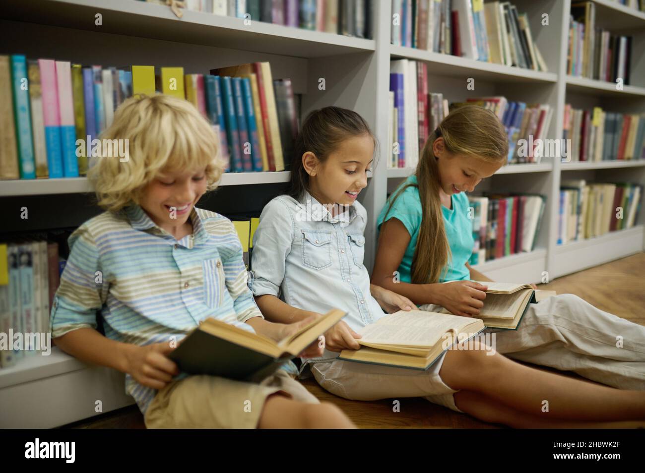 Boy and two girls sitting on floor reading books Stock Photo