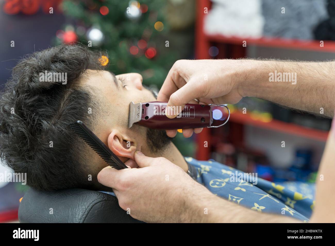 A barber use clipper to cut a gentleman's sideburn hair in barber shop