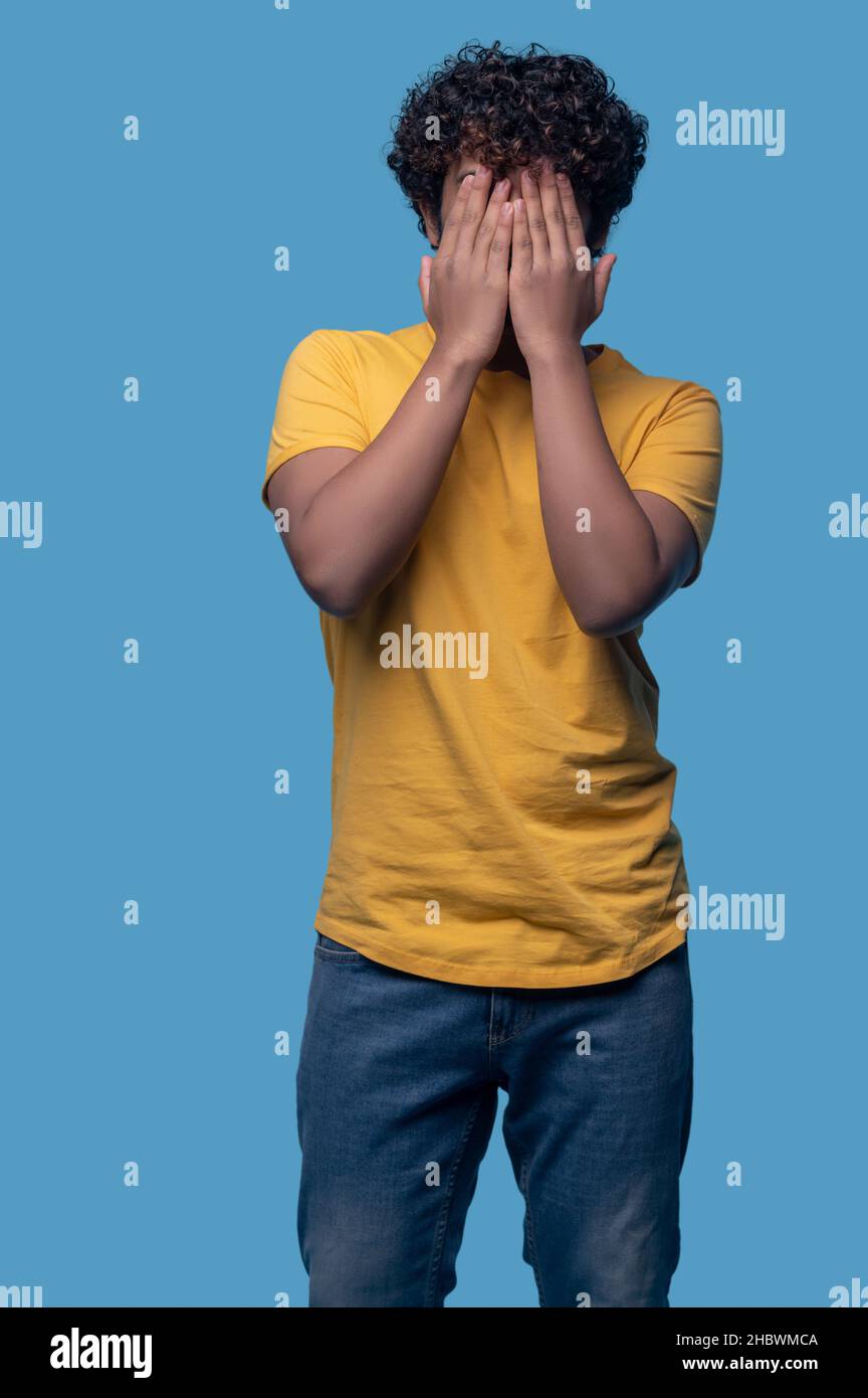 Dark-haired male doing a facepalm against the blue background Stock Photo