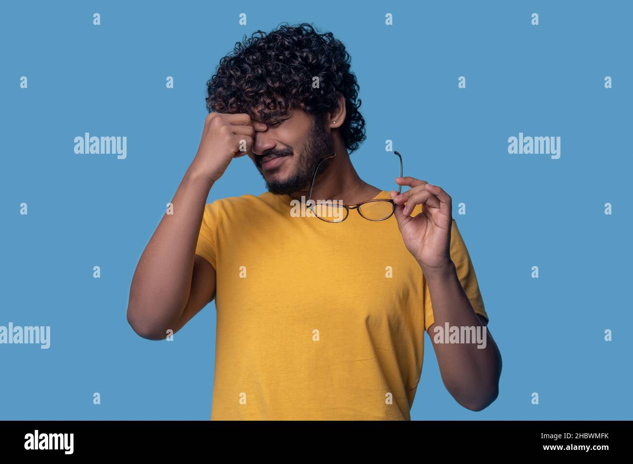 Tired curly-haired bearded guy suffering from eyestrain Stock Photo