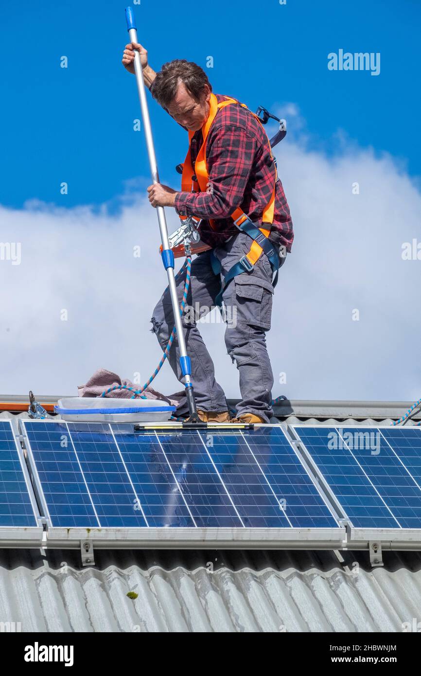 Tradesman cleaning solar panels on roof of house Stock Photo