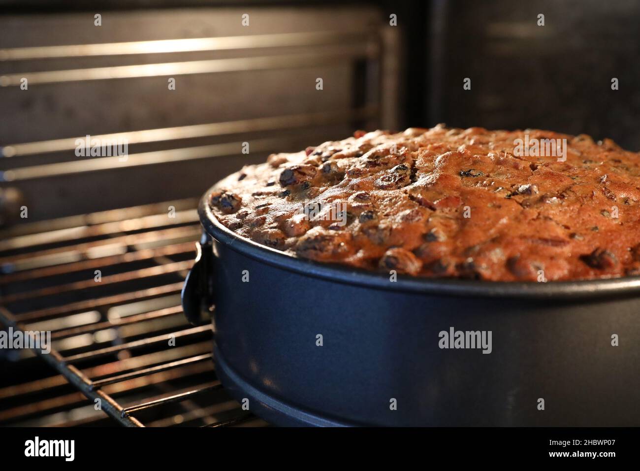 A close up of a delicious golden brown traditional fruit or festive Christmas cake still in the oven. Round baking tin and oven tray with perfectly co Stock Photo