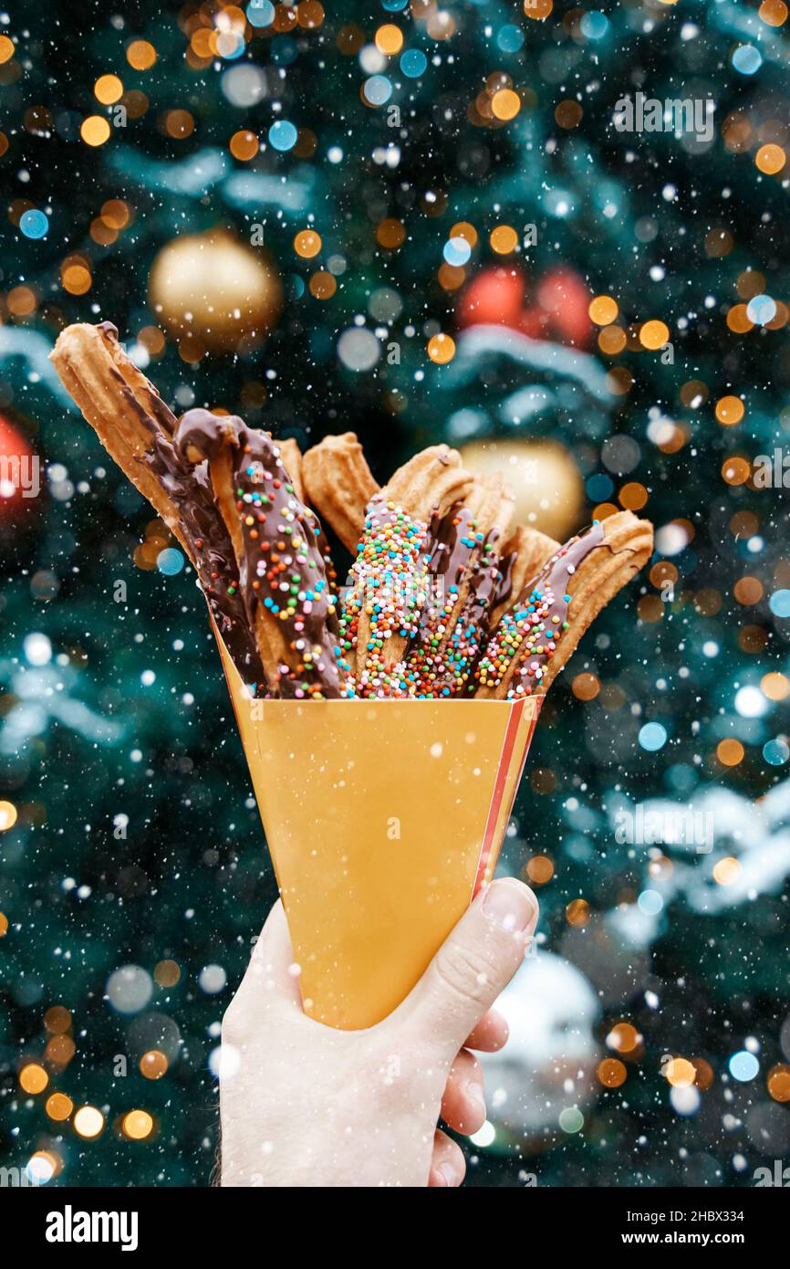 Churros waffles in a hand on the winter snow market. Churros Mexican street food dessert. Fast food sweets, Christmas fair cookies. High quality photo Stock Photo