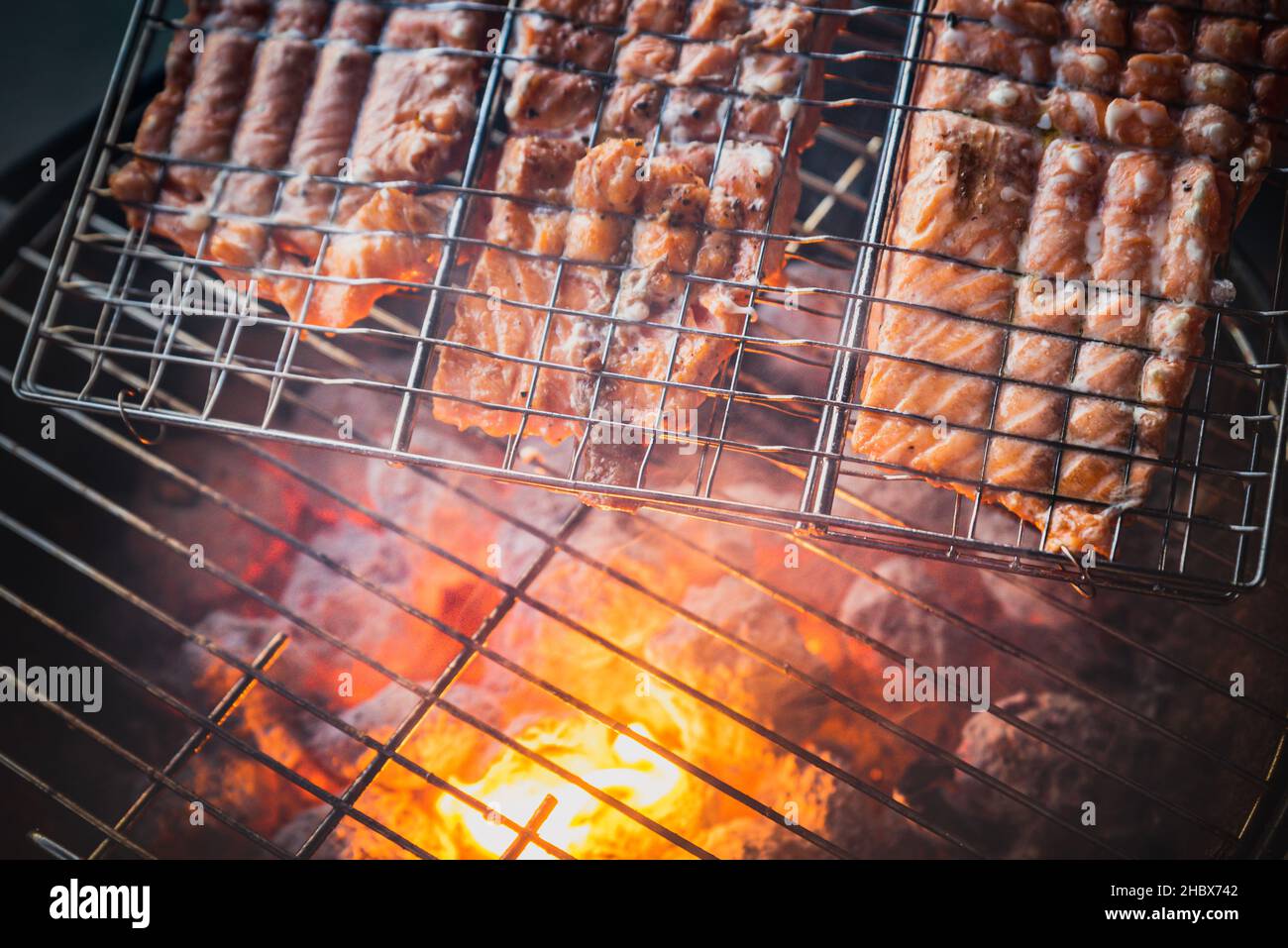 Outdoors: Salmon being grilled with live fire or burning charcoal in a BBQ bowl. Top or aerial view of red hot flame roasting raw steaks of fat fish Stock Photo
