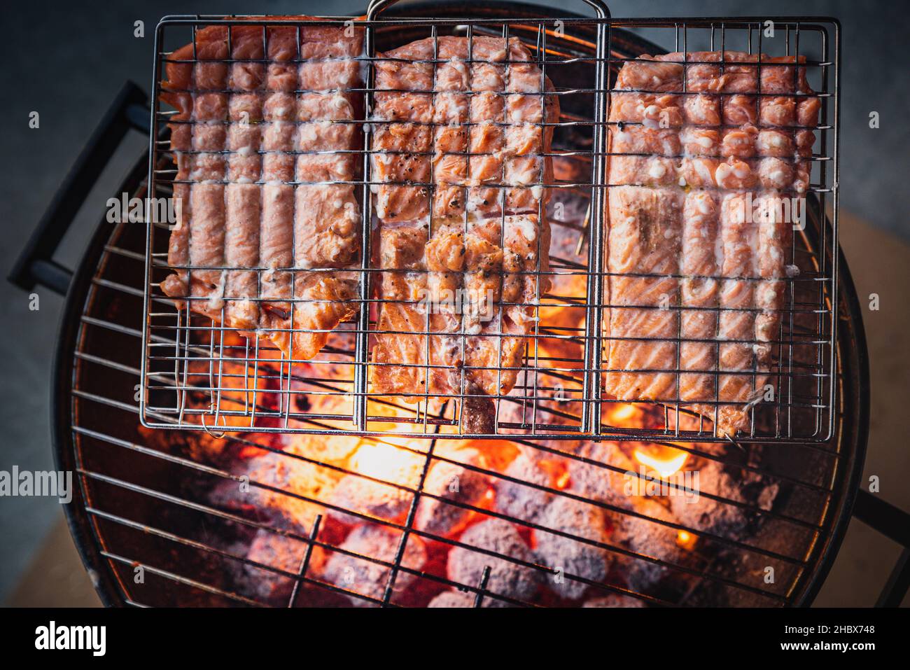 Barbecue detail with fresh row Salmon being grilled or roasted on burning hot carbons, viewed from above. BBQ melting fish in a grill on live fire Stock Photo