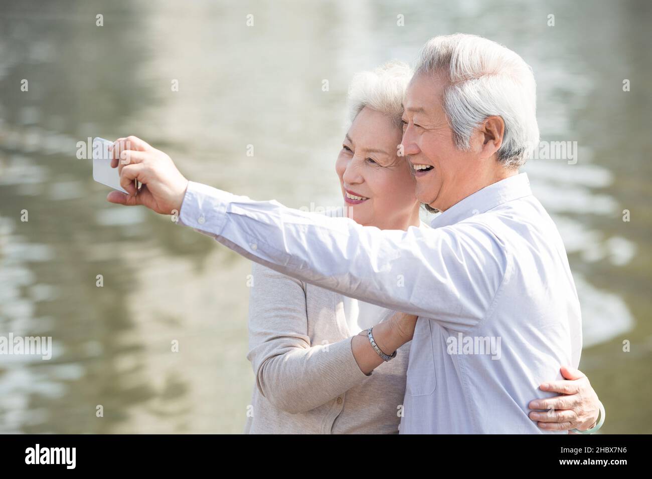 Happy elderly couple taking selfies on their mobile phone by a lake Stock Photo
