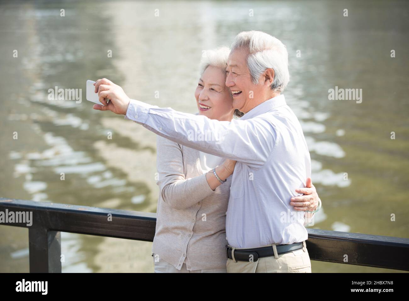 Happy elderly couple taking selfies on their mobile phone by a lake Stock Photo