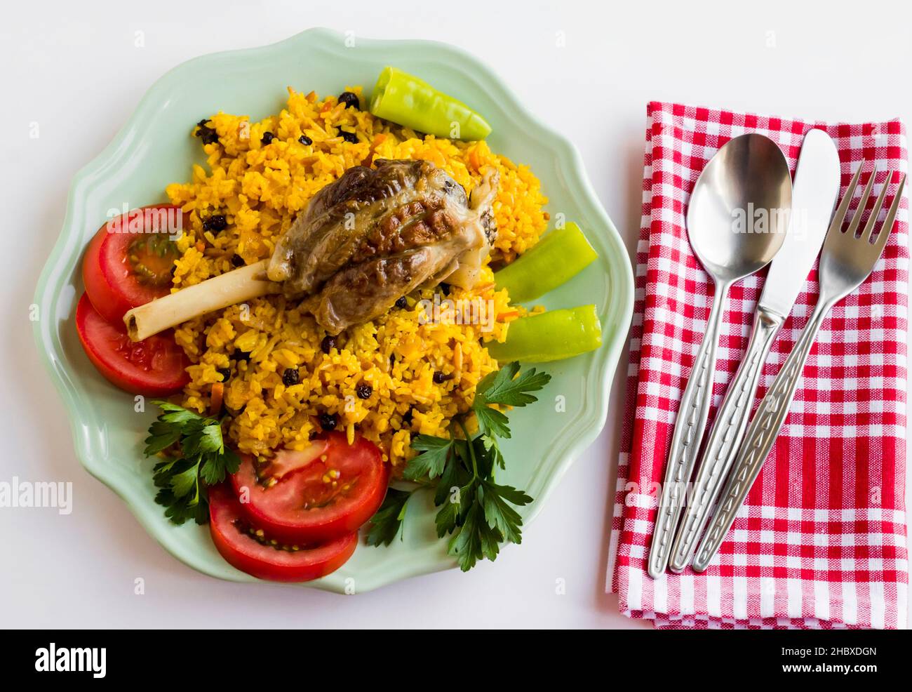 Traditional Arabic rice,pilaff with lamb shank in plate,on white surface with metal cutlery set and red fabric napkin.The Sacrifice Feast Concept Stock Photo
