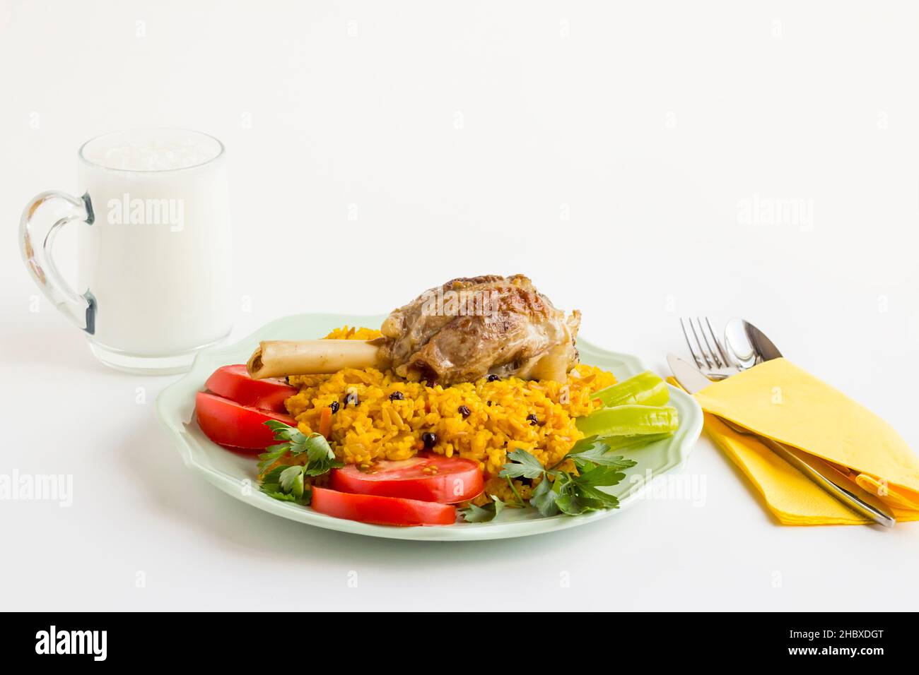 Traditional Saffron Arabian Rice,pilaff with lamb shank in plate,on white surface with cutlery set,napkin and drink.The Sacrifice Feast Concept Stock Photo