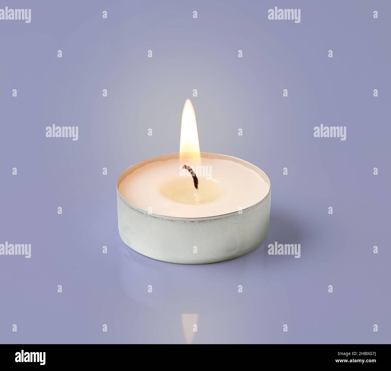 burning tea light candle isolated on violet background Stock Photo