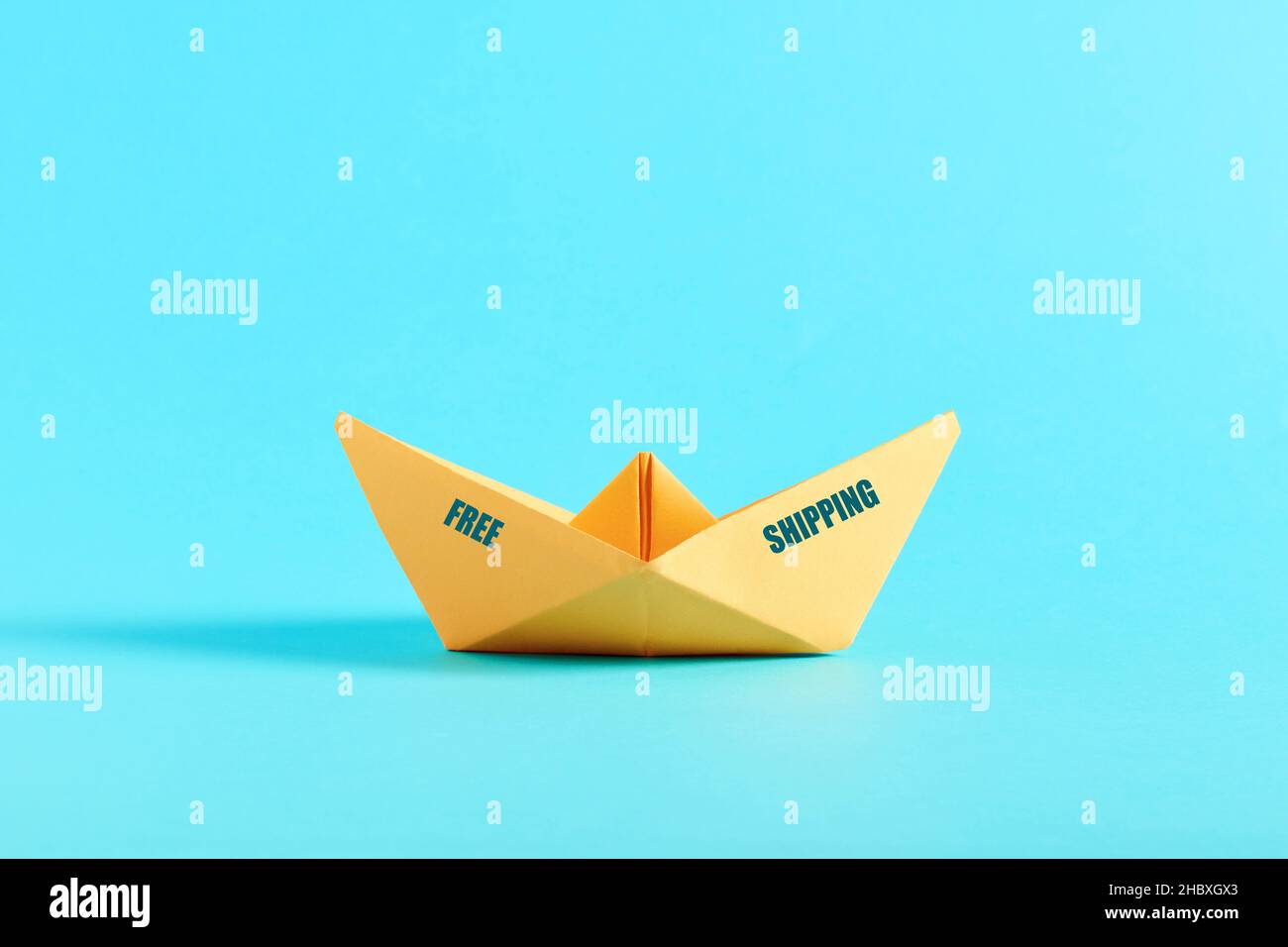 Yellow origami paper ship with the message free shipping on blue background. Free shipping on orders concept. Stock Photo