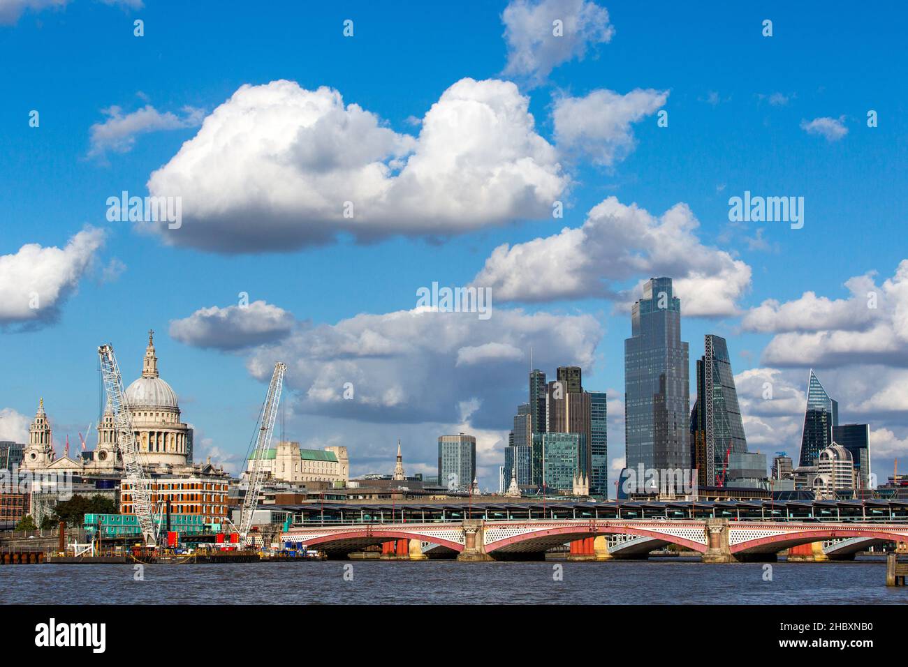 view from bridge of St. Pauls Cathedral and glass tower buildings in London with blue sky and big clouds and construction cranes Stock Photo