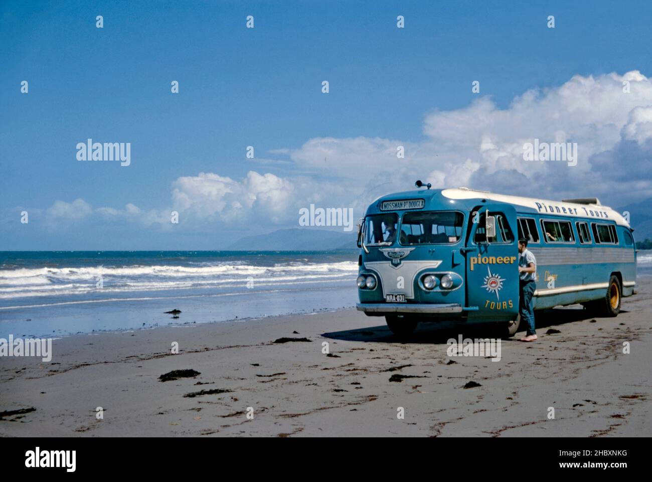 A coach of Pioneer Tours on a Pacific Ocean making a stop on a beach north of Cairns, Queensland, Australia in 1966. The destination board indicates the blue bus is on its way to Mossman and Port Douglas. In 1947 Pioneer Tours, part of the RM Ansett organisation imported a Flxible Clipper from the Flxible Company in Loudonville, Ohio, USA. After evaluation, Ansair Pty Ltd, also part of Ansett, obtained a licence to build the Clipper in Australia. Ansair built 131 right-hand-drive ‘Ansair Flxible Clippers’ between 1950 and 1960, both for the Ansett organisation and other operators. Stock Photo