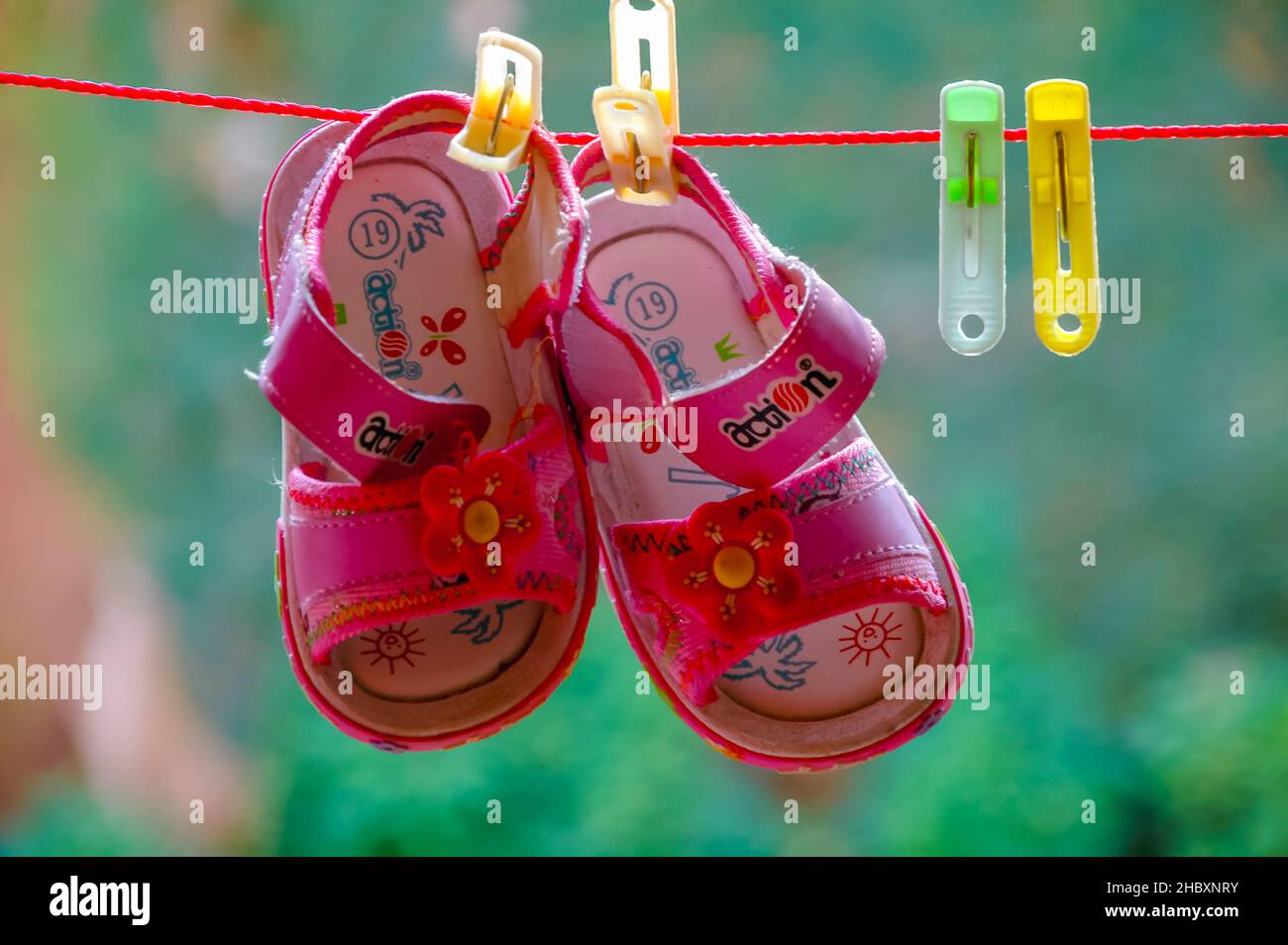 A pair of decorative pink baby sandals / shoes, washed and hanged up on a clothes line for drying, using plastic clothespins or clothes pegs. Stock Photo