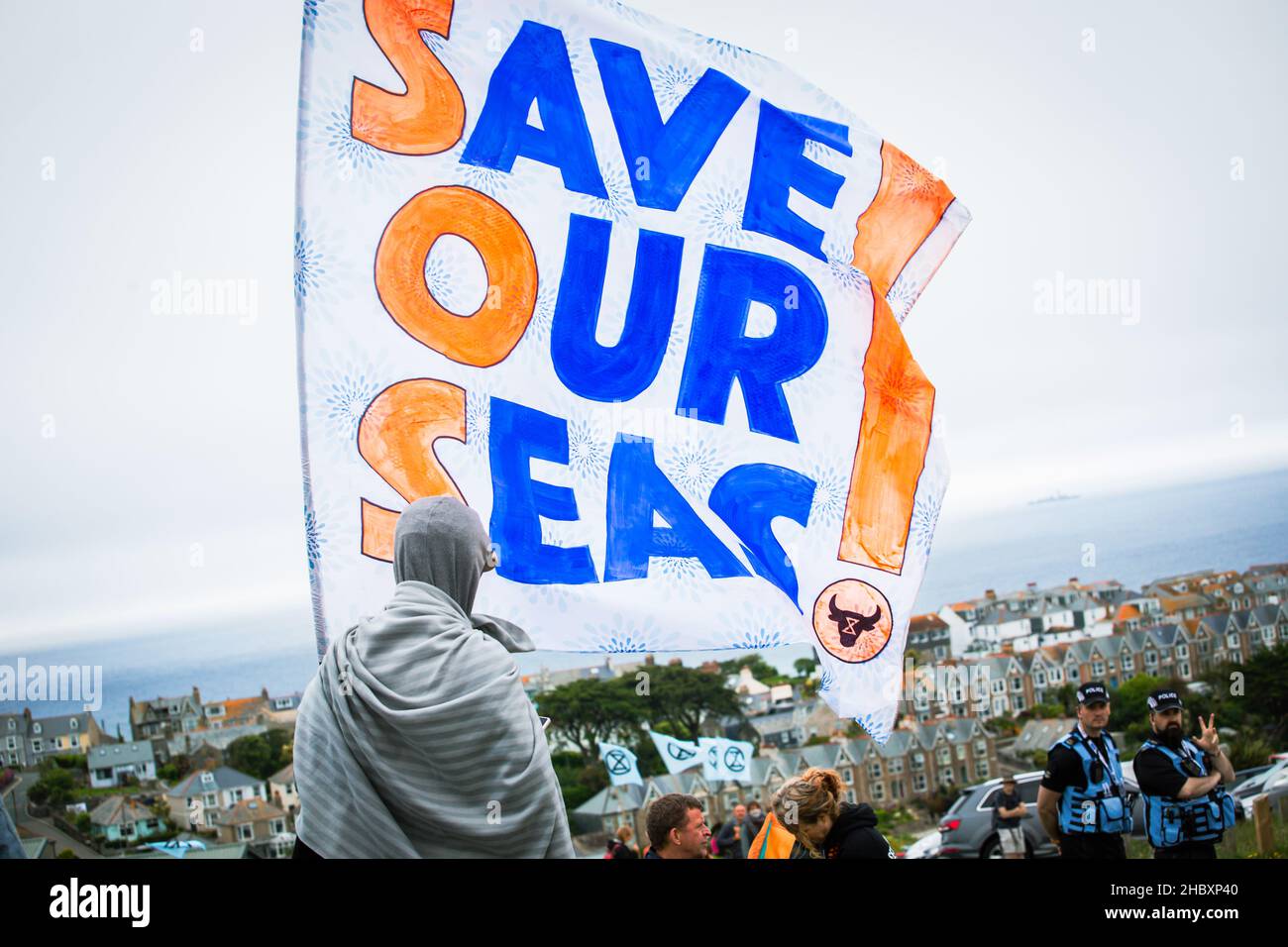 animal rebellion protestor holding large Save our Seas flag overlooking view of Cornwall at G7 protest June 2021 Stock Photo
