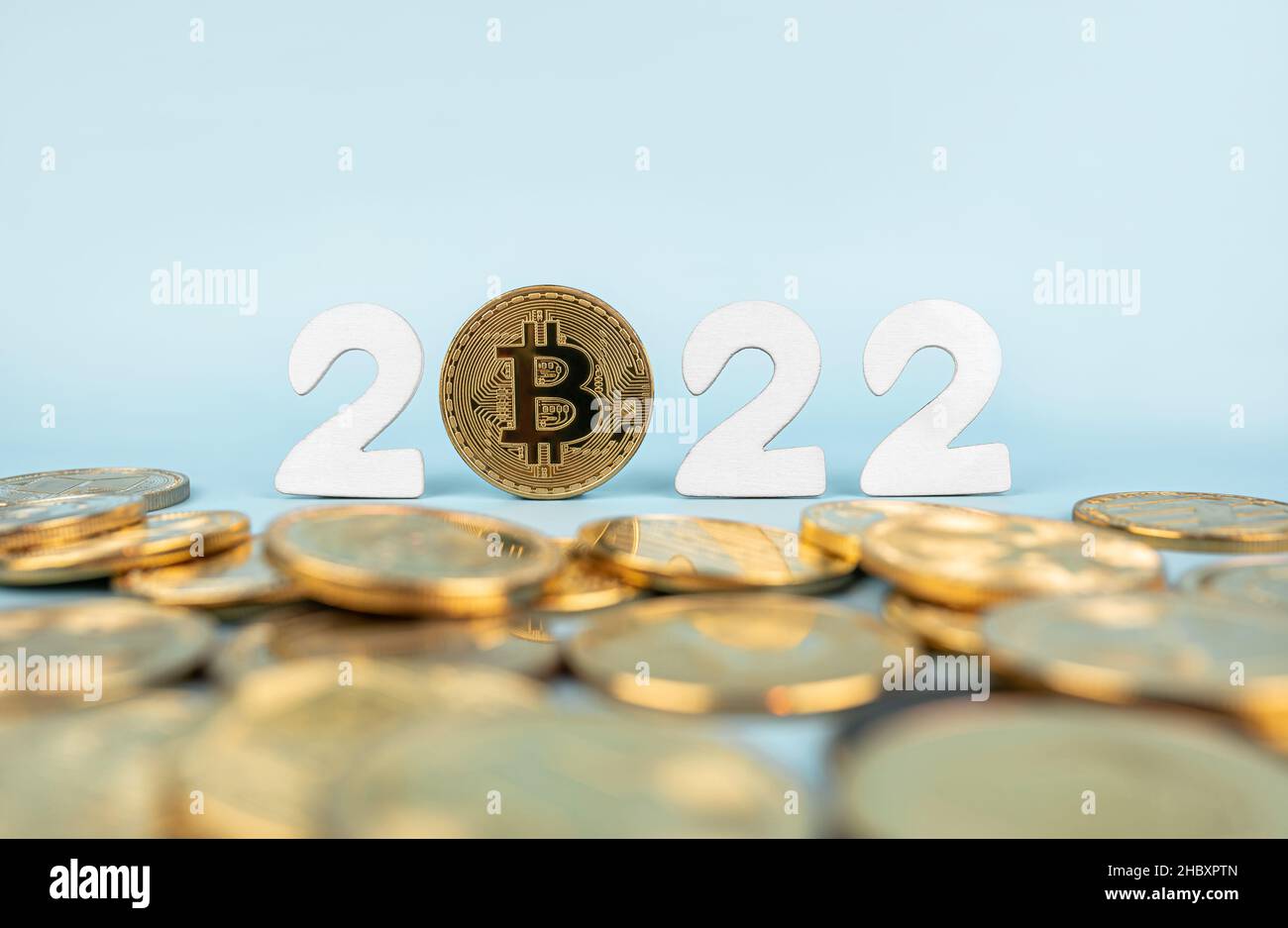 Bitcoin 2022 price prediction concept. Btc coin standing next to cryptocurrency tokens and year numbers on blue background. Close-up, soft focus. Stock Photo