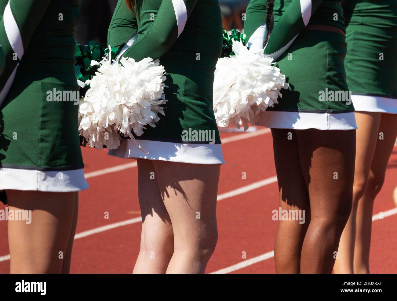 Close up of cheerleaders in green uniforms holding white pom poms behind backs. Stock Photo