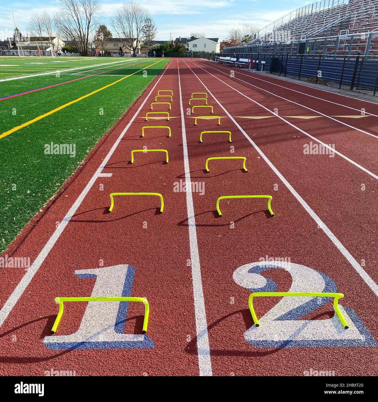 Looking down at two rows of eight yellow mini hurdles set up on a red track at the 100 meter start line. Stock Photo