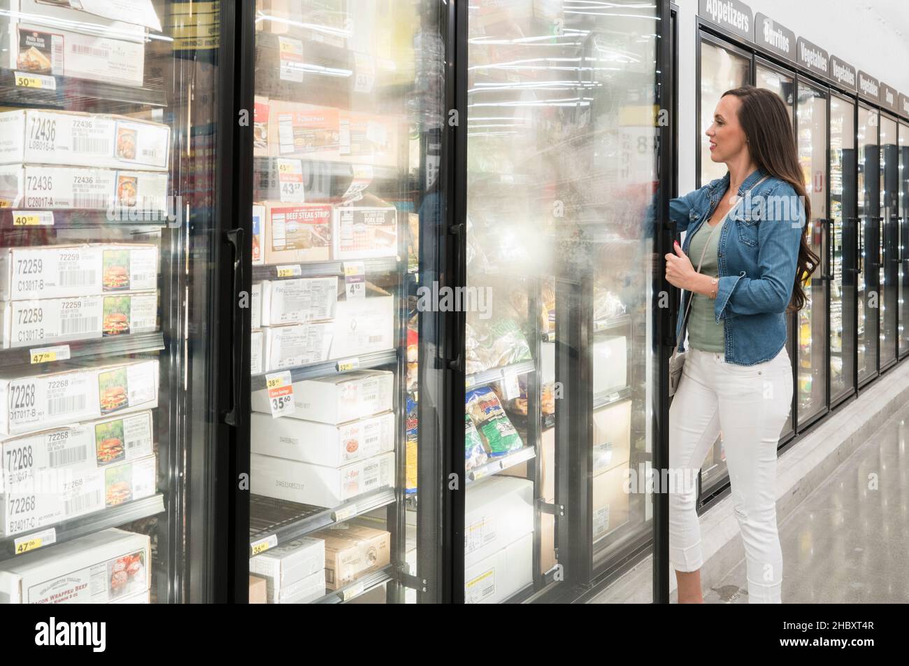 Woman opening freezer compartments in a supermarket, grocery shopping