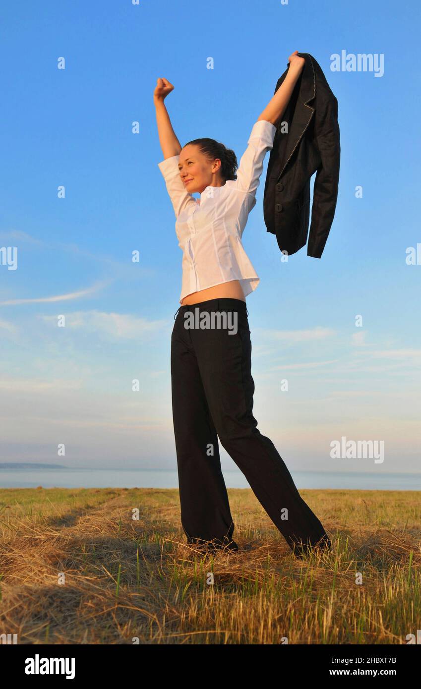 Happy businesswoman with arms raised holding suit jacket walking on sandy beach, freedom. Stock Photo