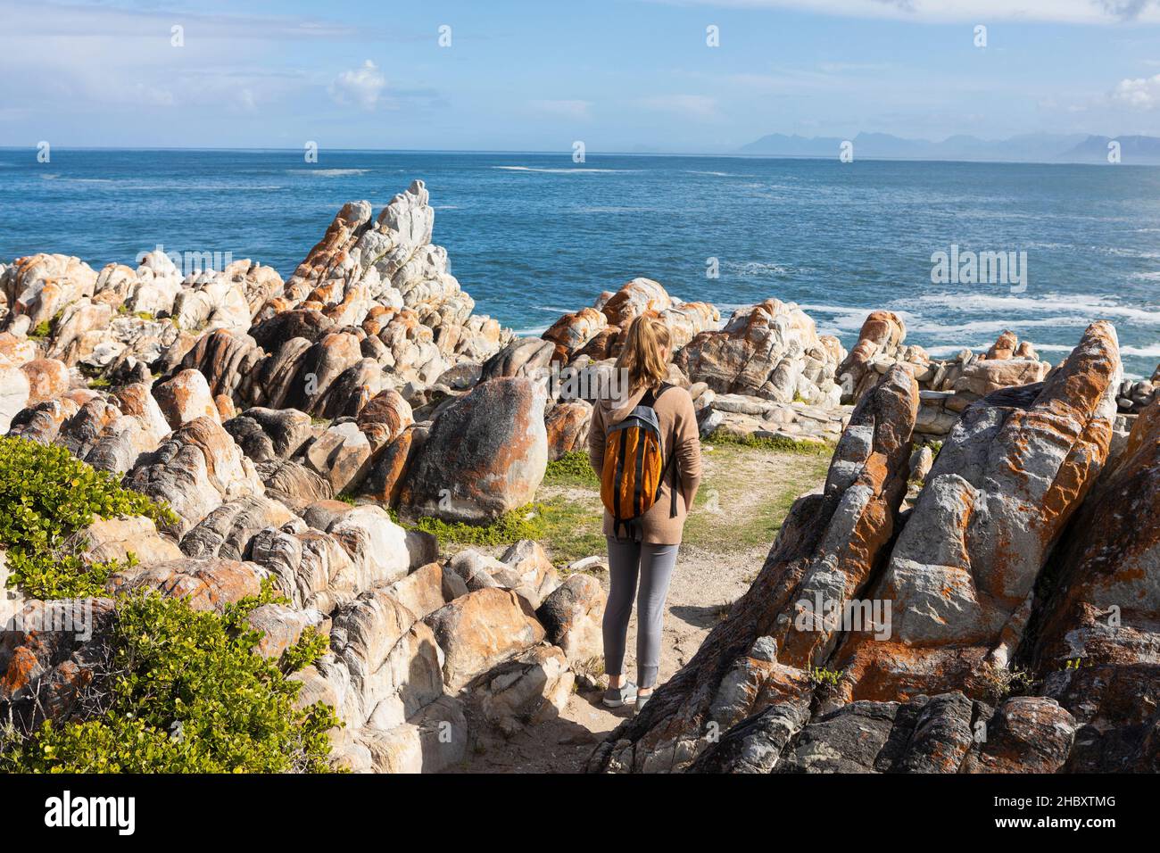 Teenage girl with a backpack standing on the rocks looking over the ocean Stock Photo
