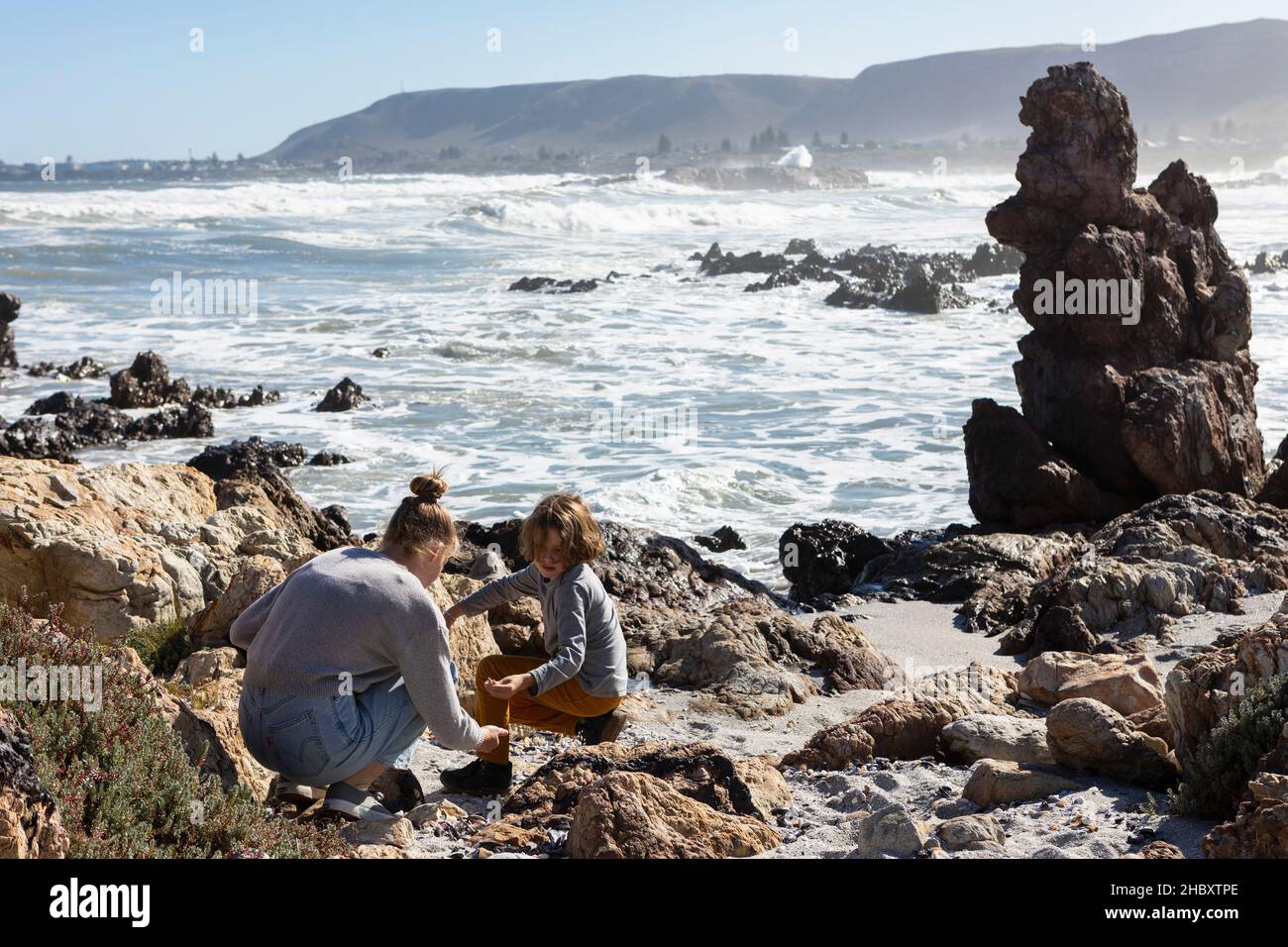 Teenage girl and a boy exploring the rocks and surf, sea fret rising off the breaking waves of the ocean. Stock Photo