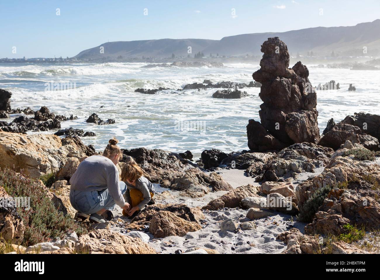 Teenage girl and a boy exploring the rocks and surf, sea fret rising off the breaking waves of the ocean. Stock Photo