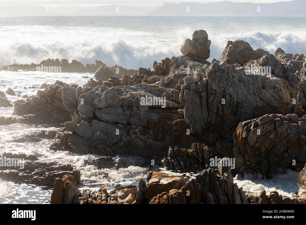 Jagged rocks on the shore at De Kelders, tall waves rolling in and breaking on the rocks Stock Photo