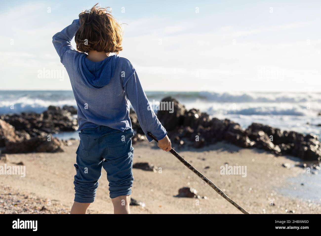 Boy playing on a rocky beach, holding a long kelp seaweed strand Stock Photo