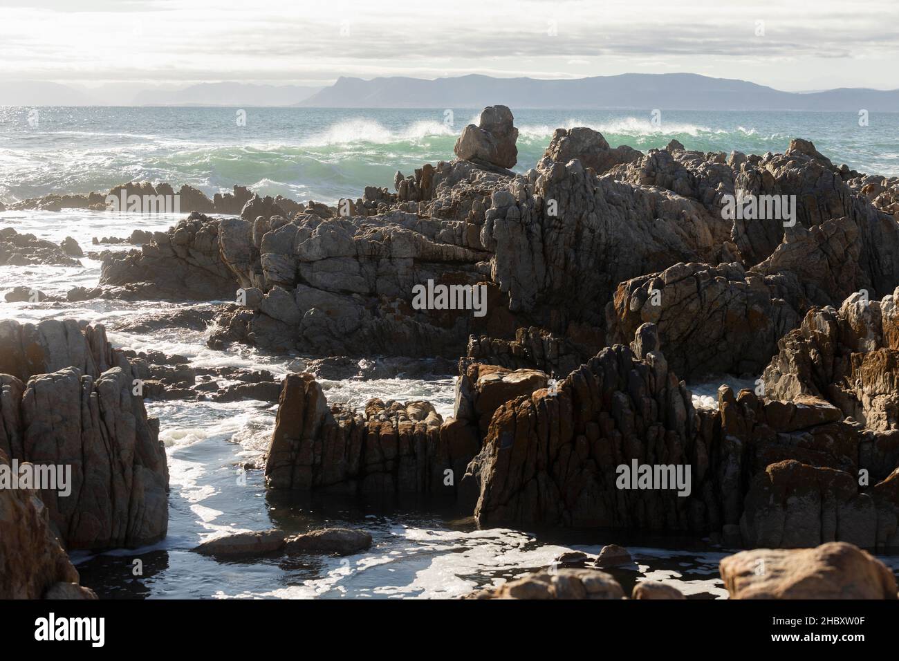 Jagged rocks on the shore at De Kelders, tall waves rolling in and breaking on the rocks Stock Photo