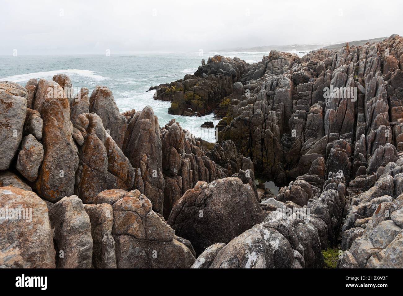 Jagged rocks and the rocky coastline of the Atlantic at De Kelders beach, waves breaking on shore. Stock Photo