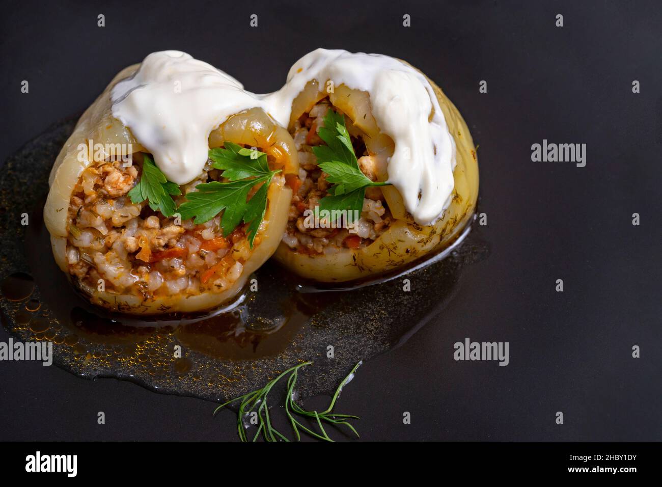 2 stuffed yellow bell peppers, with minced pork meat, rice, carrots and onion, sour cream on top, isolated on black background. Stock Photo
