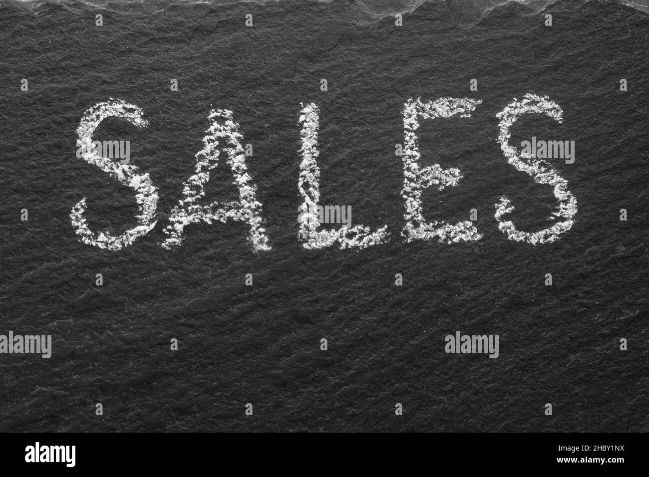 Sales written with white chalk on black stone texture. Macro texture text. Stock Photo