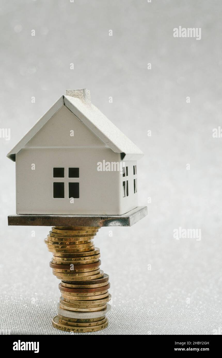 miniature metal house standing on a high stack of golden coins, creative concept Stock Photo