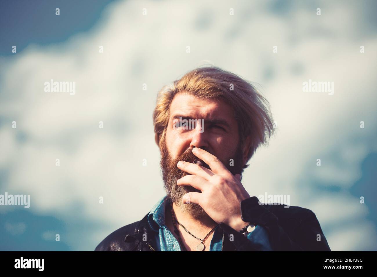 Fashion man smoking on sky background. Fashion smoker with cigarette on fresh air. Stock Photo