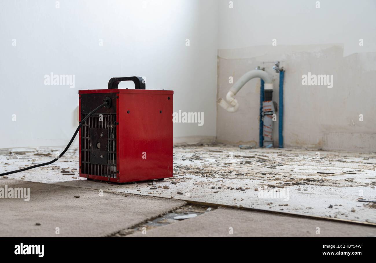 red fan heater at a construction site, remnants of tile adhesive and drain pipes in the background Stock Photo