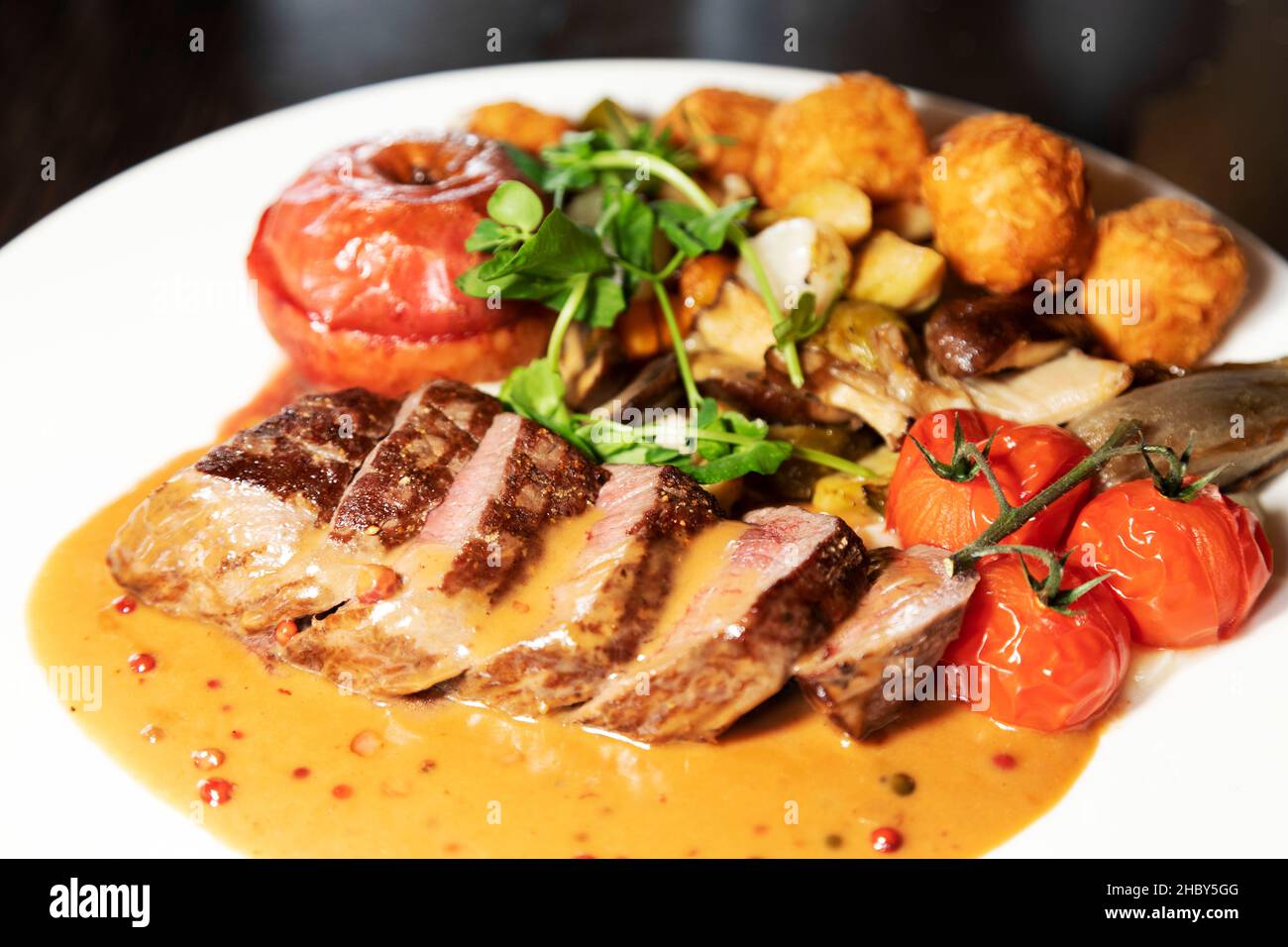 Roast wild boar served with gravy, baked apple, grilled tomatoes, seasonal greens and almond crusted potato balls. Stock Photo