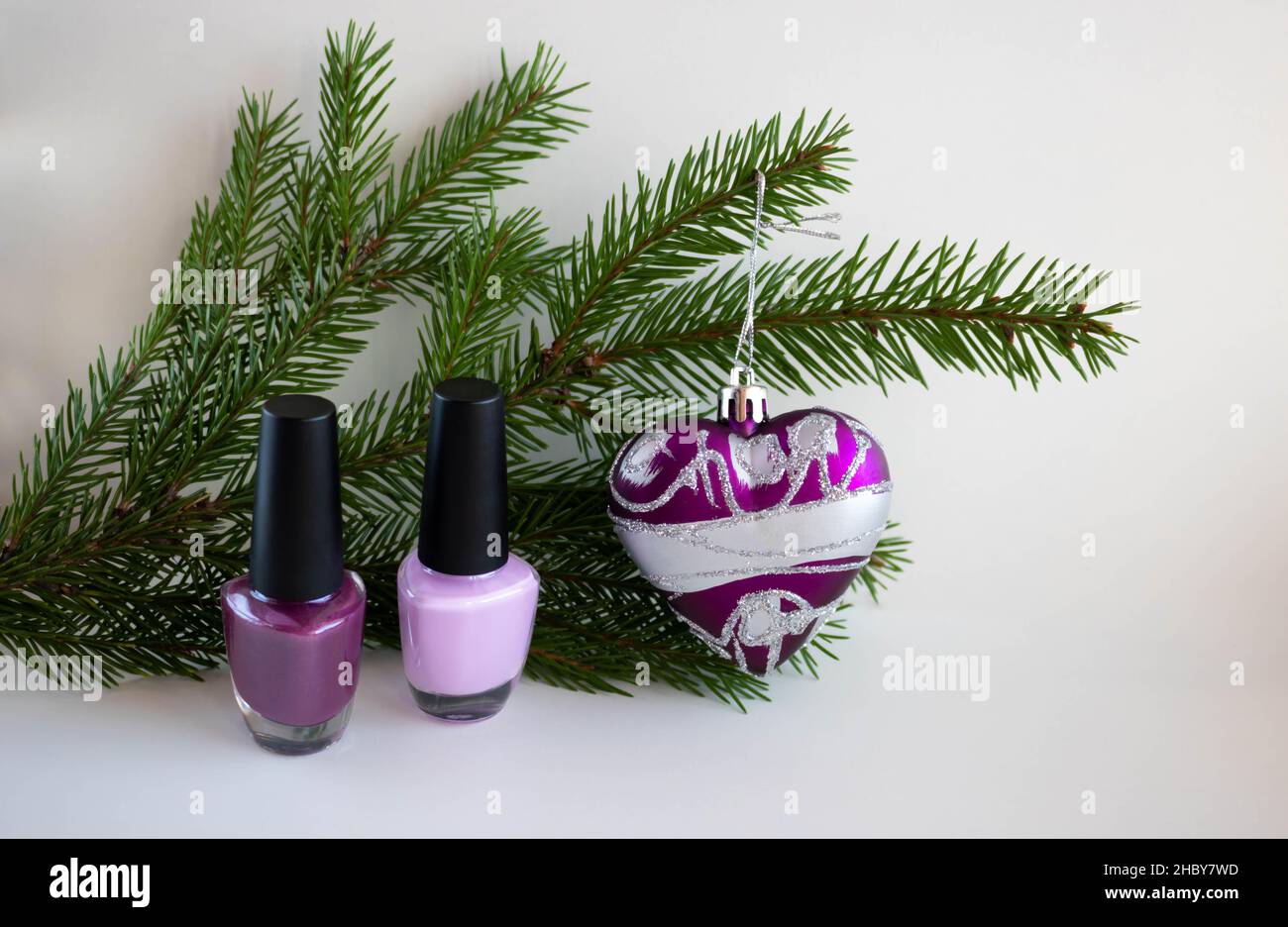 On a white background, a green fir branch, lilac lacquer and a lilac toy heart. New Year's concept. Stock Photo