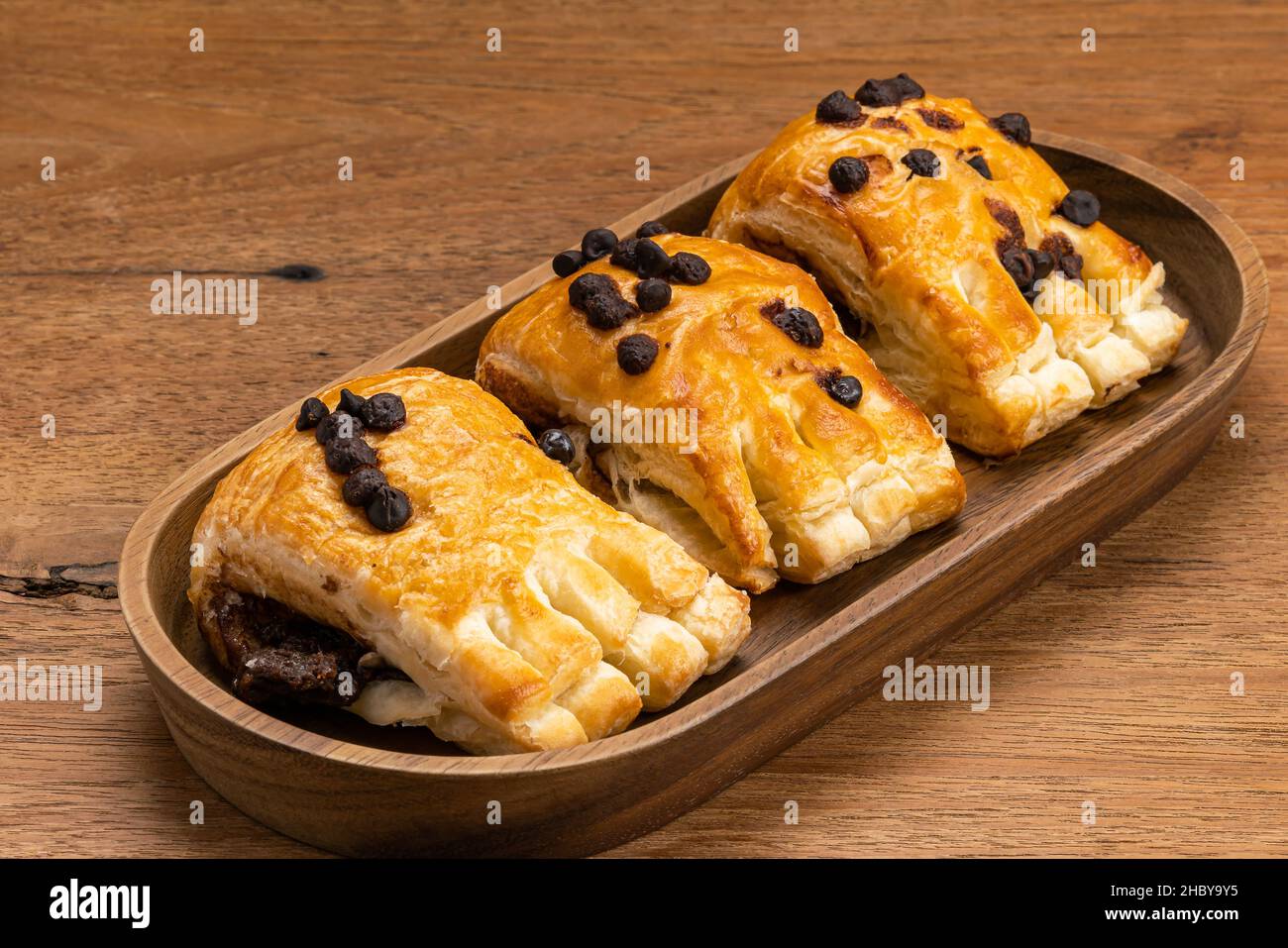 Sweet homemade Danish Pastry with chocolate cream filling topping with chocolate chips in wooden tray on wooden table. Stock Photo