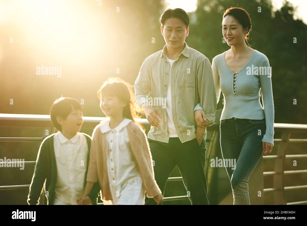 happy asian family with two children walking on pedestrian bridge in city park Stock Photo